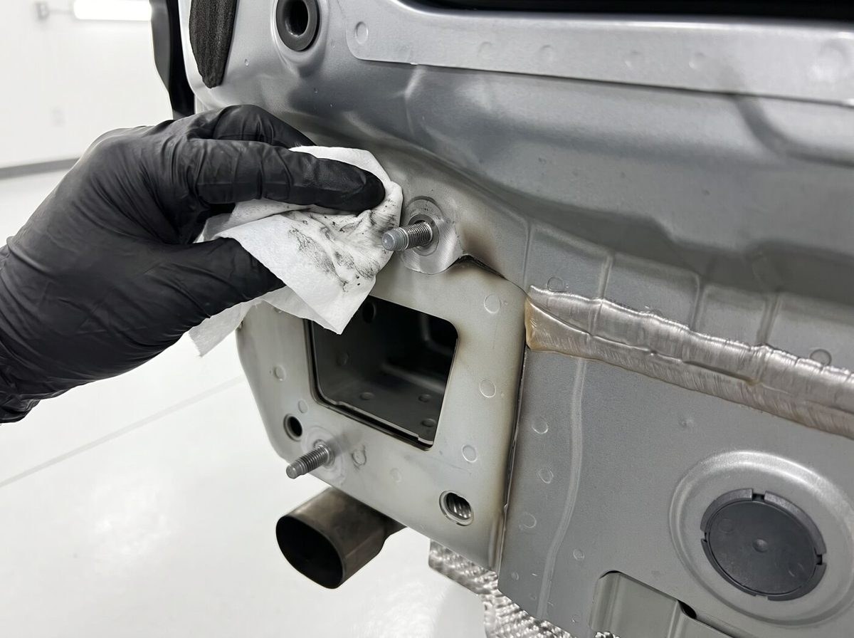 Technicien en gants prépare un point d'ancrage sur le châssis avant pose d'attelage