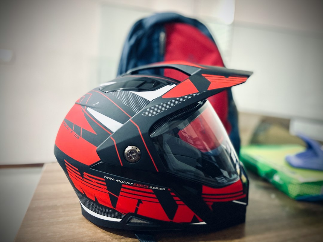 Casque de moto cross rouge et noir pose sur une table, sac a dos en arriere-plan